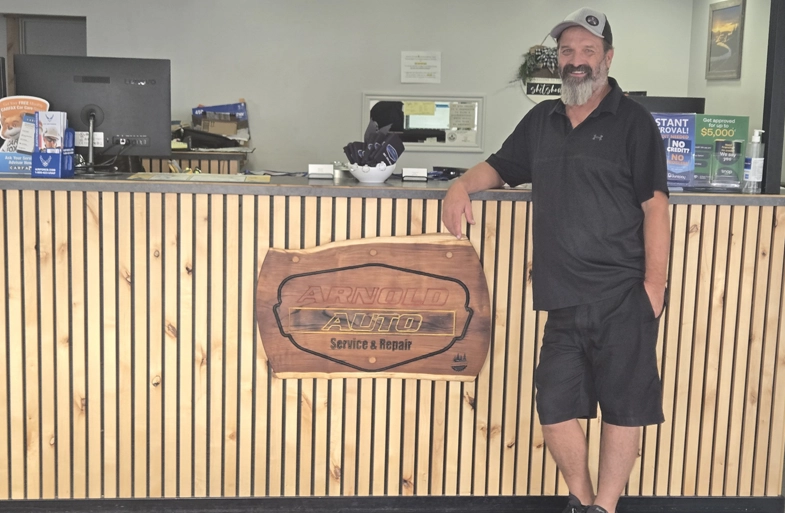 Man in a black outfit leaning on the reception counter with Arnold Auto Service & Repair sign.